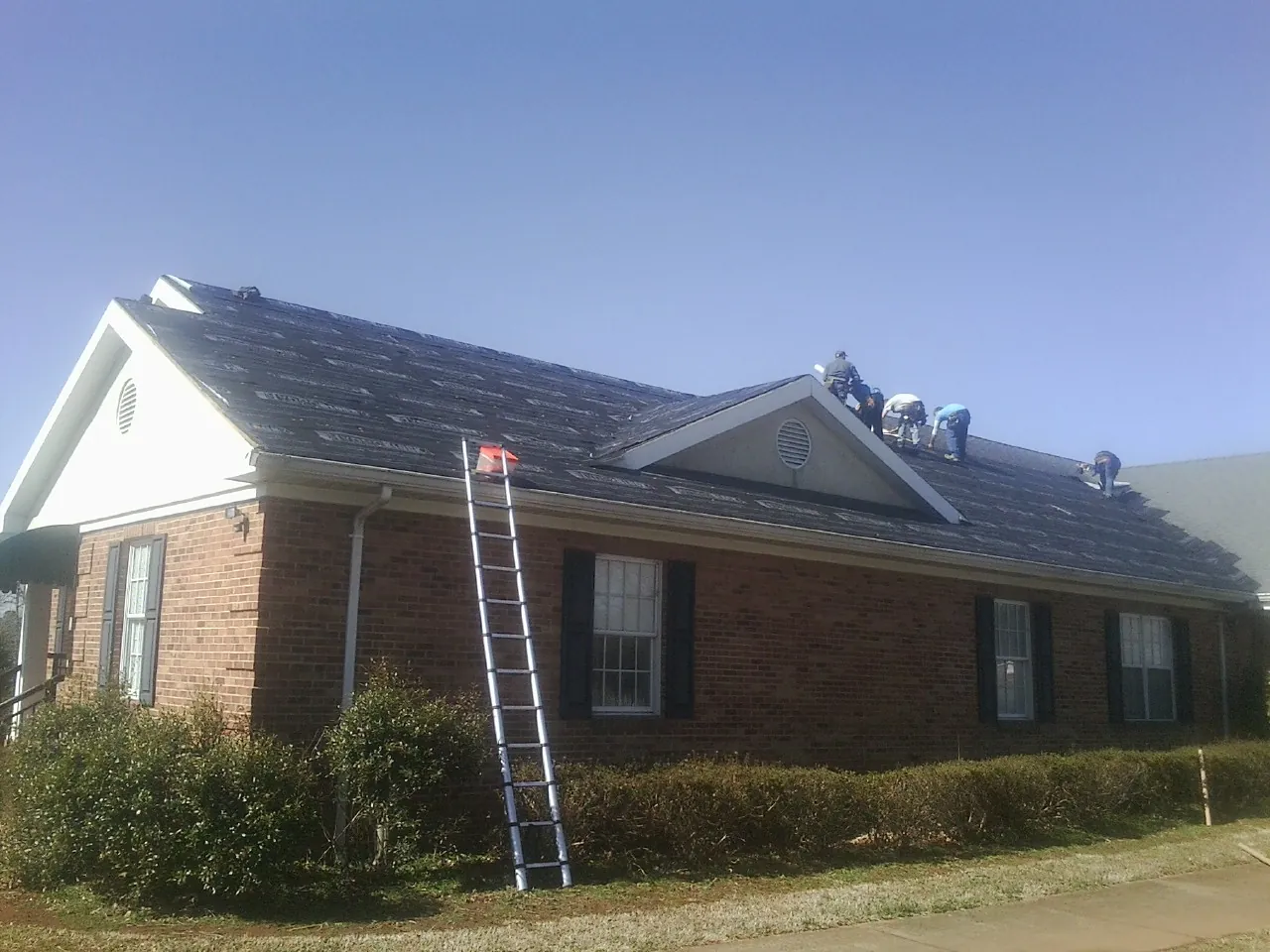 Crew tearing shingles off a brick ranch roof with a ladder set — Metal Roof Repair work by our crew in Alvarado
