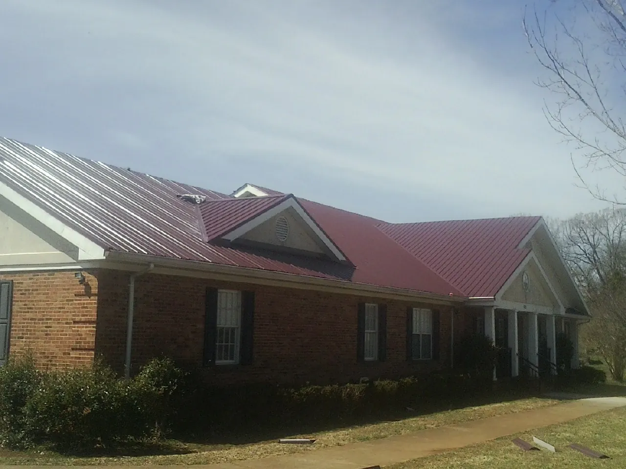Red metal roof with gabled entries on a long brick building, from a Hail Damage Roof Repair job in Alvarado