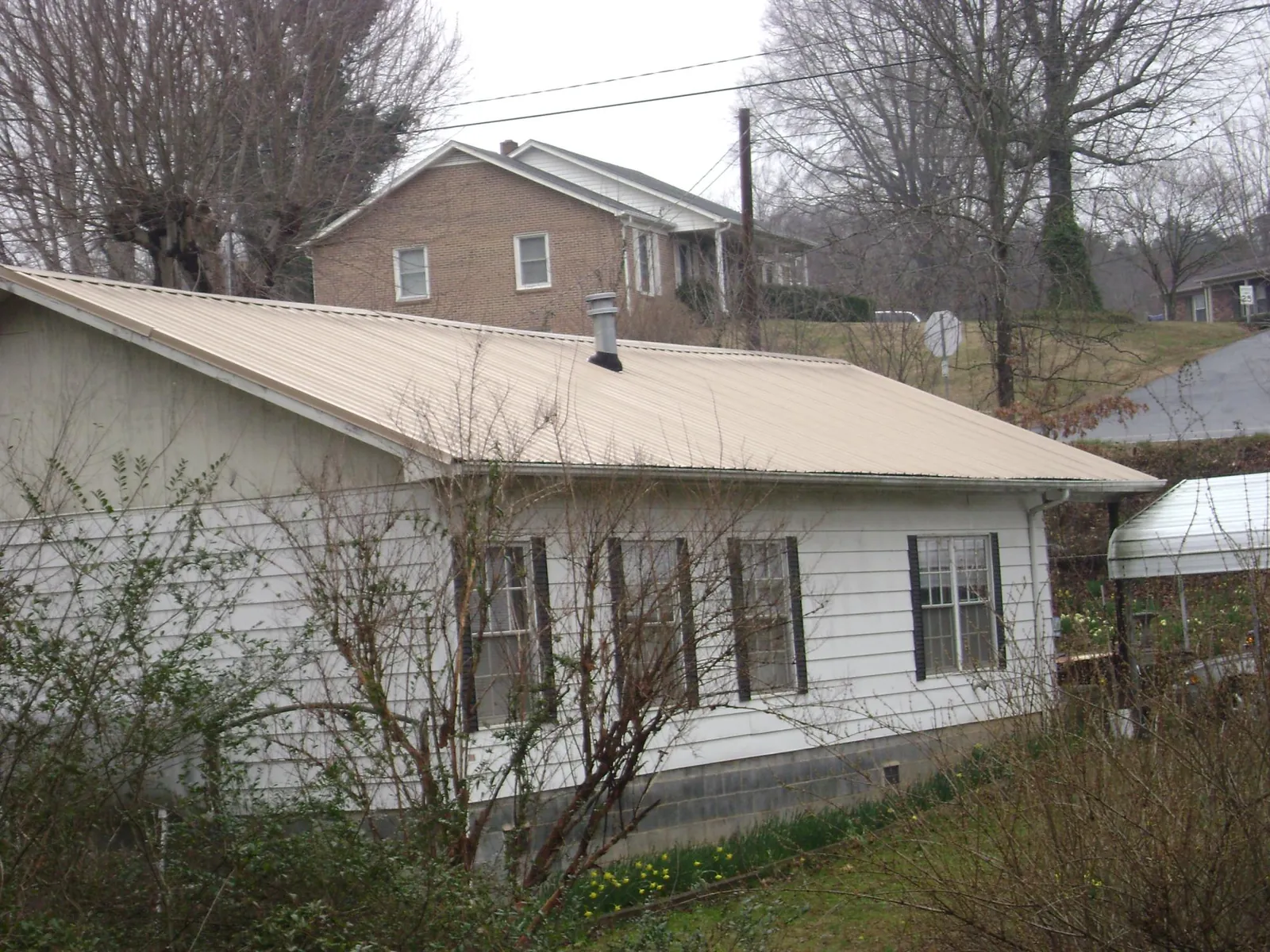 Tan metal roof on a white sided house set into a hillside — Commercial Roofing by Roofing Brothers in Alvarado